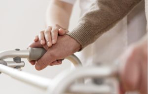 A caregivers hand resting a senior mans hand while he's using a walker to assist him with moving around