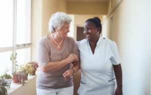 Female caregiver helping a female patient walk down a hallway