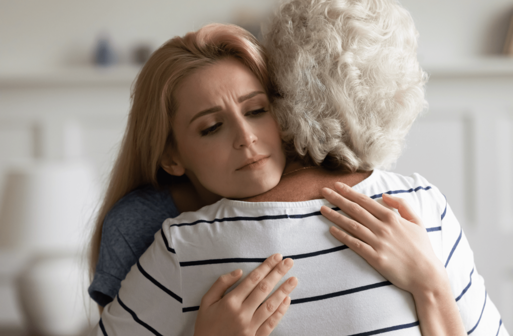 A daughter caregiver hugging her grey-haired mother with a look of fatigue in need of an independent living community