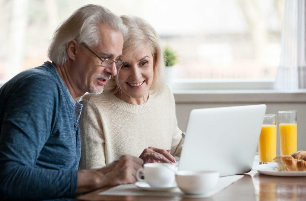 A senior couple seated down with some coffee in front of a laptop both looking at the screen while they research possible retirement communities to move into