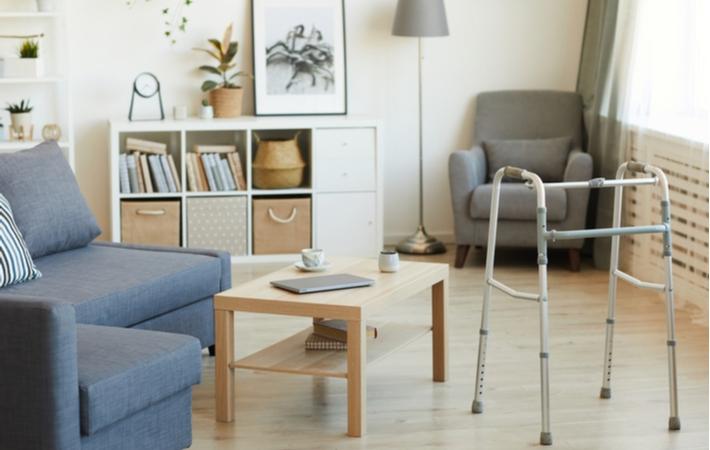 A room in a senior living community with a blue couch, coffee table and an assisted walker in front of a white cabinet and a grey chair