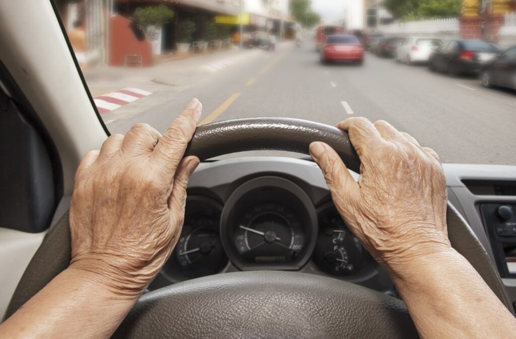 A behind the wheel perspective of a senior grabbing the steering wheel of a car while they drive in the city