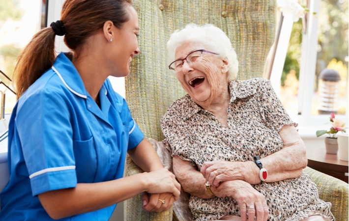 Senior woman sitting in a chair and talking with a nurse in an assisted living community