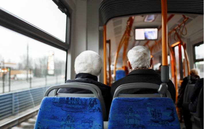 A view from behind of a senior couple sitting on a bus using the transportation service provided by their independent living community