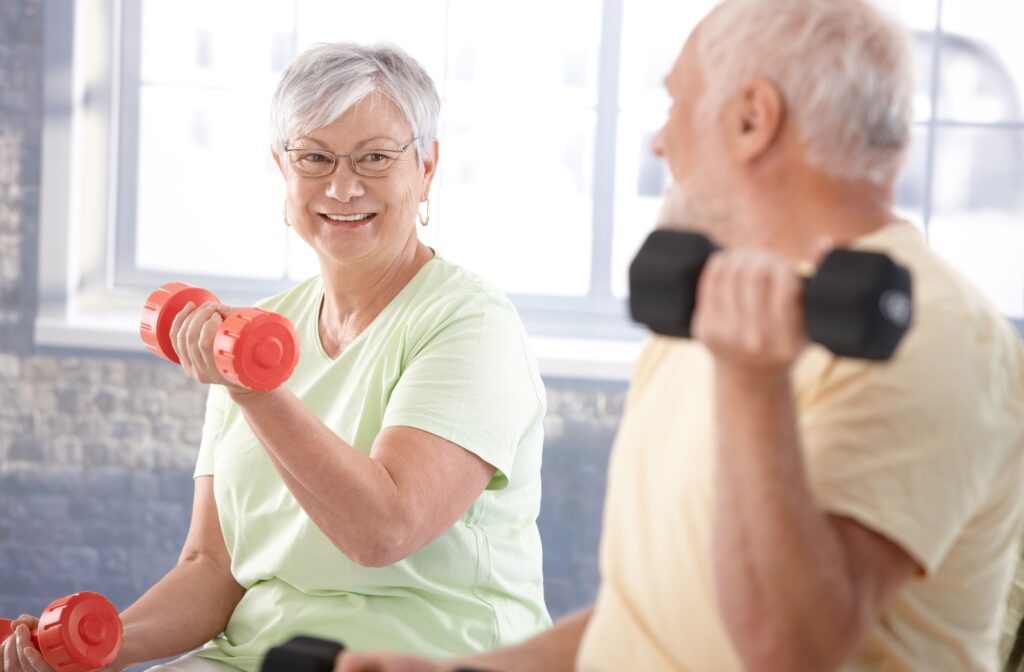 A senior couple looking at each other smiling while they use colourful dumbbells to do bicep curls
