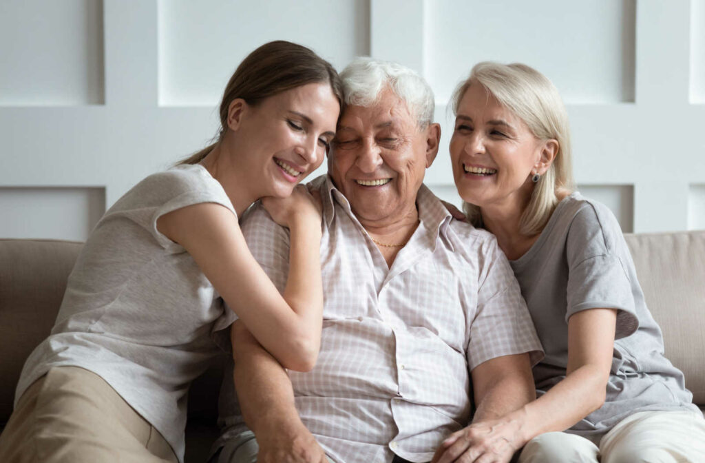 A daughter and her aging parents smiling while enjoying a warm embrace sitting on a couch
