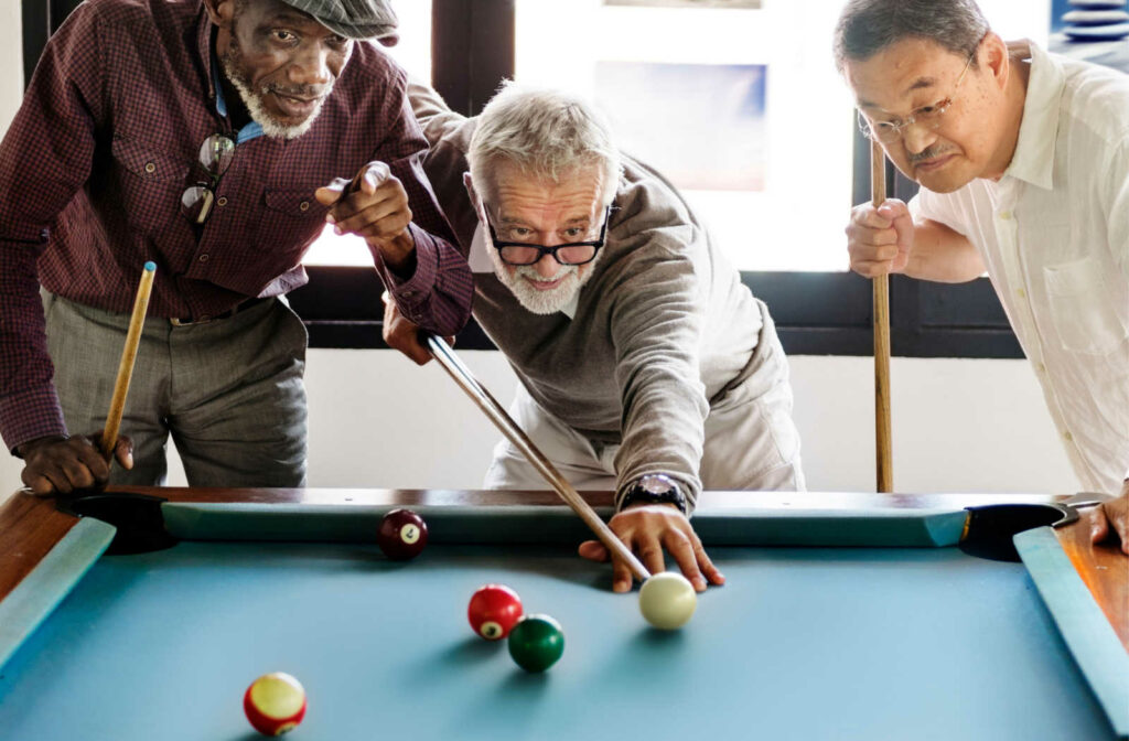 A group of three senior men enjoying a game of pool to keep themselves entertained and happy.