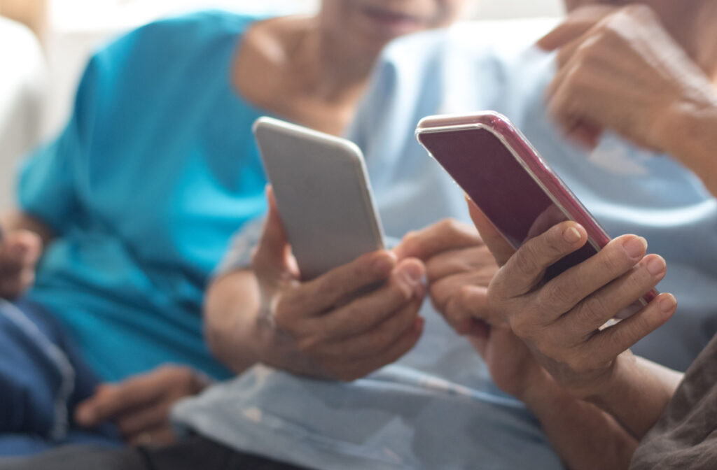 Close-up of 2 smartphones as 2 seniors hold them while sitting on a couch and show something on it to a friend.