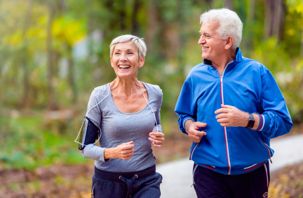 An older adult man and a woman smiling while jogging outdoors.