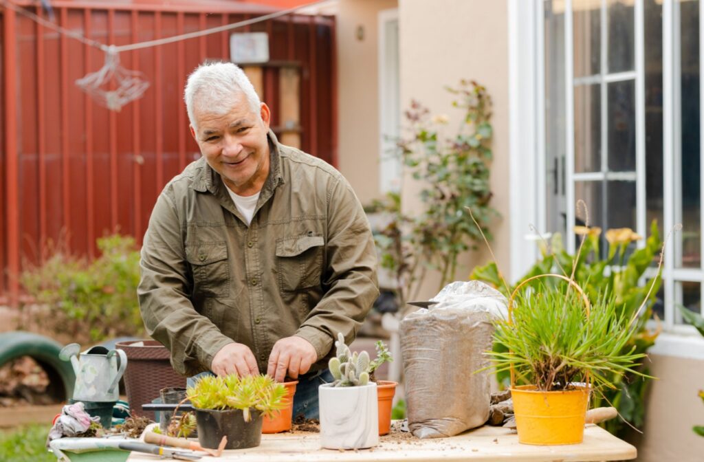 An older adult man planting potted plants, smiling and looking directly at the camera