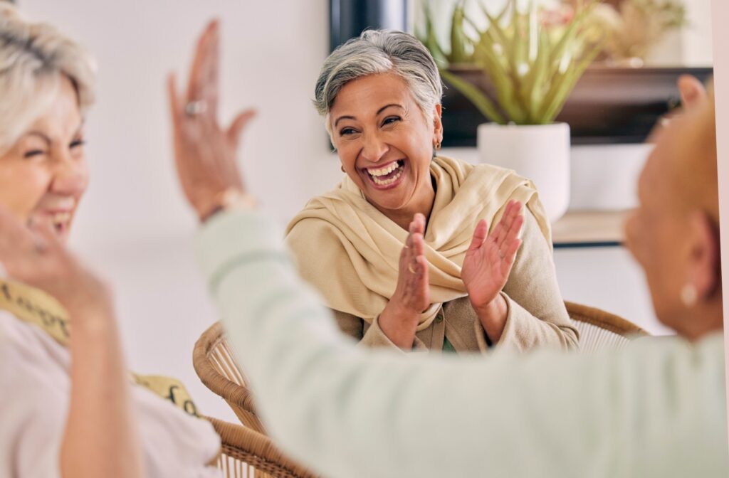 Joyful senior women laughing and clapping hands together during a social gathering.