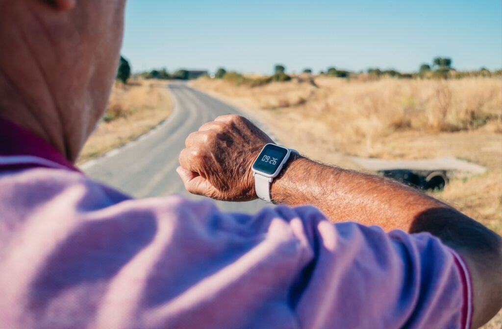 A senior raises their wrist to look at the time on their smartwatch while out for a walk on a clear blue sky day