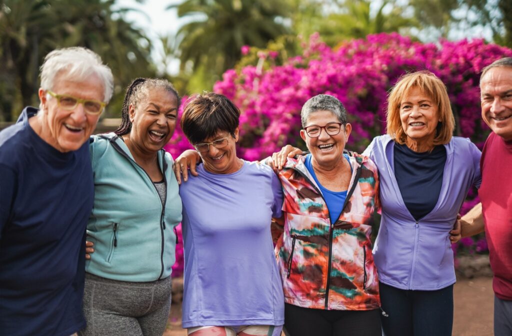 Diverse group of older adults outdoors, laughing and posing together with arms around each other.