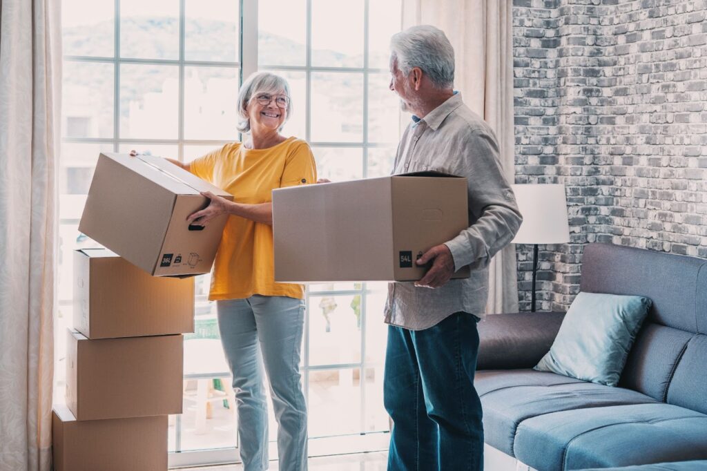 Mature couple moving into new apartment, carrying cardboard boxes into empty room.