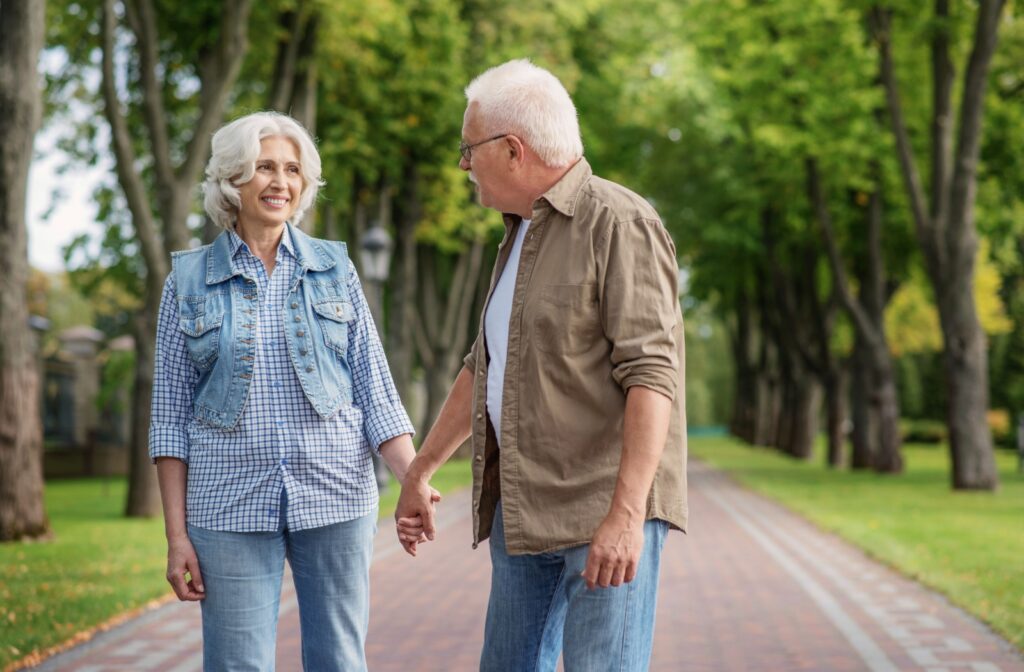 A senior couple hold hands while out for a walk in a bright green park near their senior living home