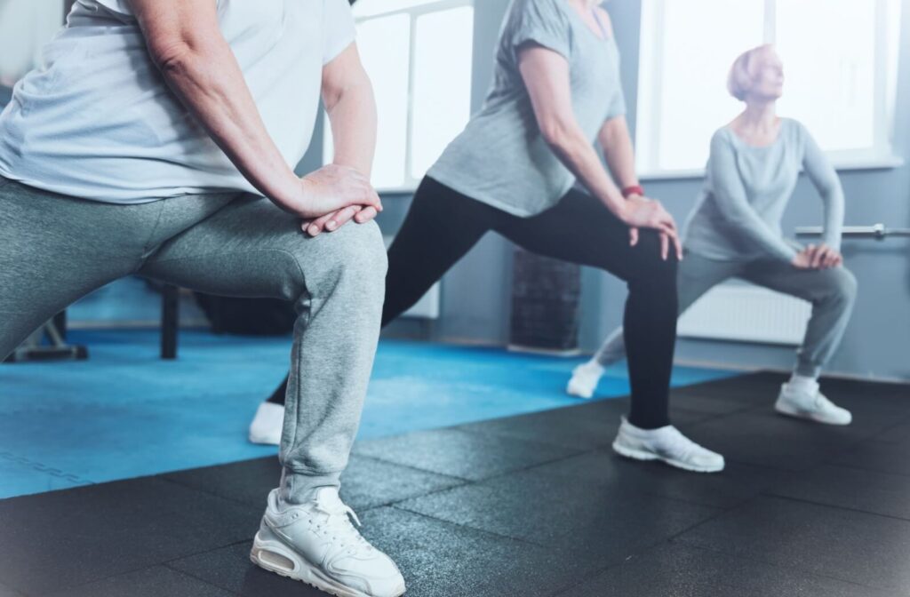 A group of three seniors stand in a row and does lunging exercises to strengthen their knees and quads.