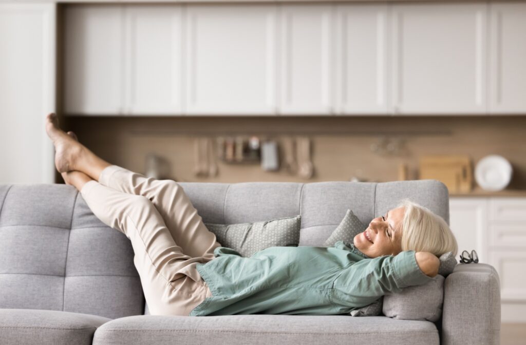 An older adult lies sideways on their couch and smiles up at the ceiling in their new retirement home