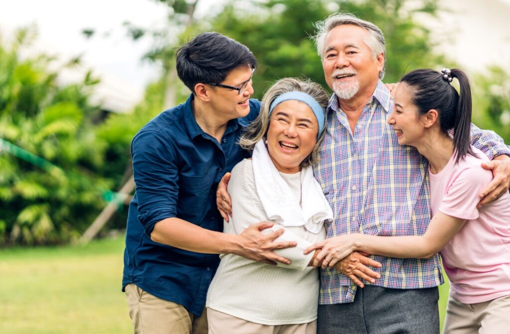 Adult siblings and their senior parents embrace each other in a bright, outdoor setting