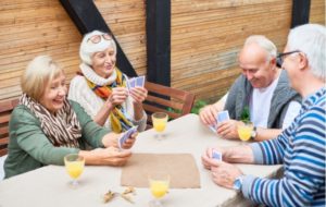 Four seniors gathered around a table socializing and playing cards outdoors